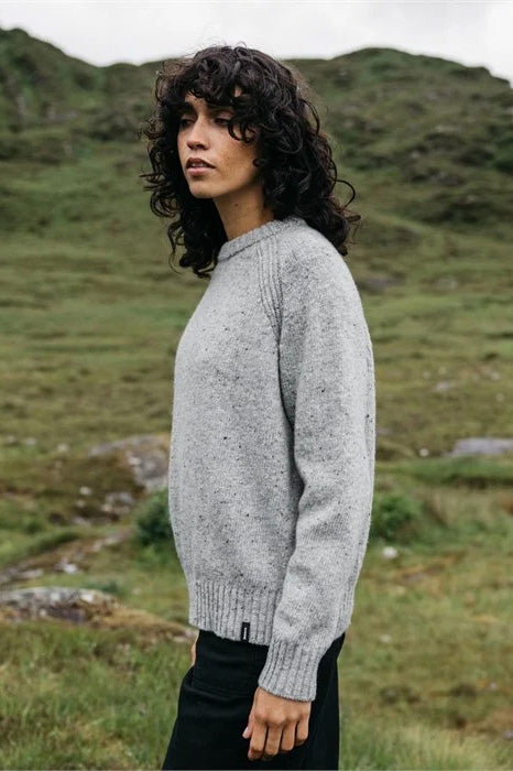 Person wearing a gray sweater standing in a grassy field with mountains in the background