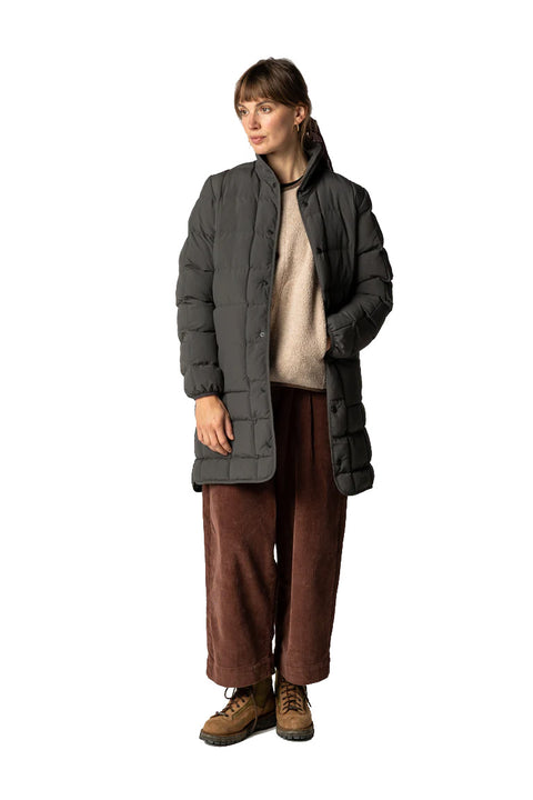 Person wearing a gray puffer coat over a black coat, brown pants, and brown shoes on a white background