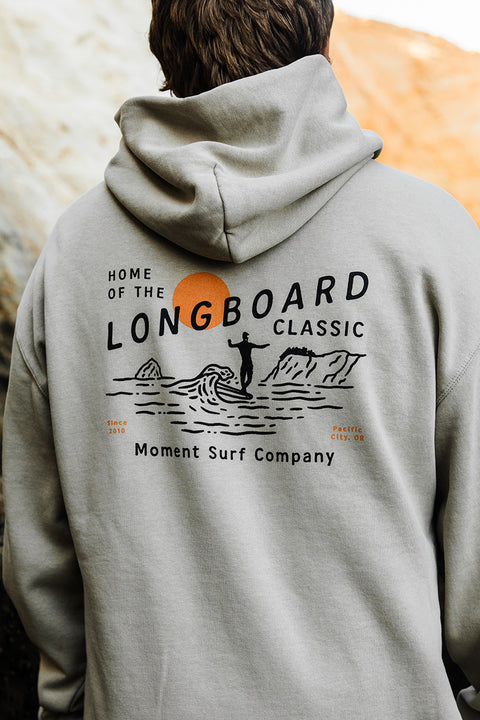 Person wearing a hoodie with 'Home of the Longboard Classic' design on the back, featuring Moment Surf Company branding.