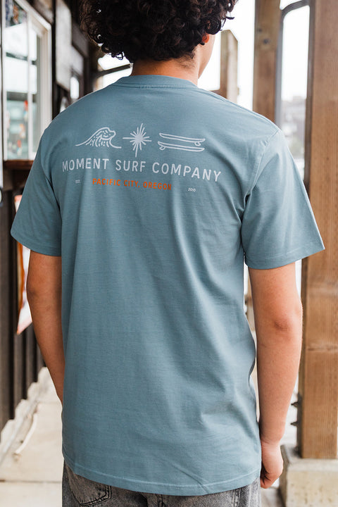Person wearing a blue t-shirt with 'Moment Surf Company' branding on the back.