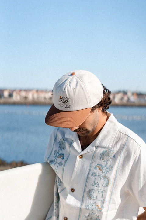 Rhythm Fern Cap - Tobacco - On a man by the ocean holding a surfboard