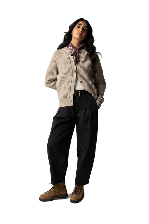 Woman wearing a beige cardigan, black pants, and brown boots on a white background