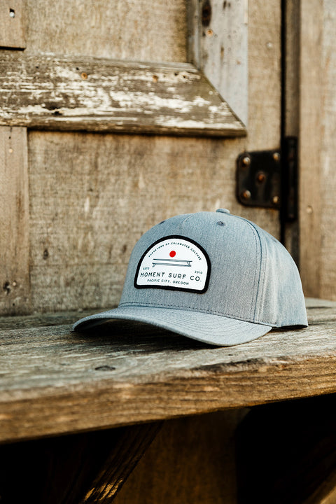 Moment Board Stack 5 Panel Hat - Grey - Sitting On a Wooden Shelf.