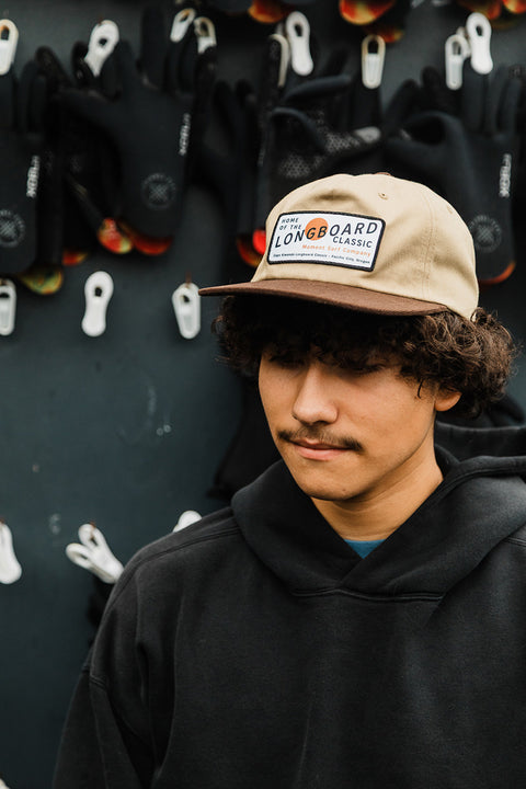 Moment The Classic 5 Panel Hat - Khaki / Brown on a model in front of wetsuit gloves