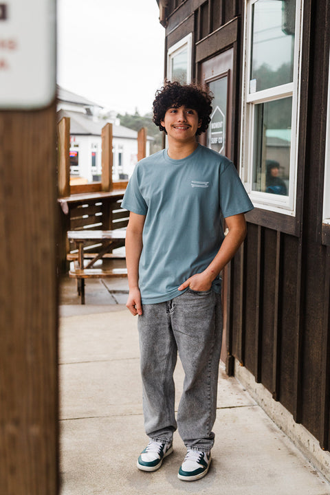 Person wearing a blue t-shirt and gray pants standing on a wooden deck.