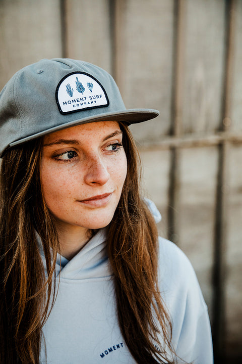 A female model looking left of the camera wearing the Moment Kelp Friends 5 Panel Hat.