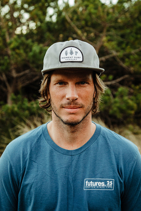 A male model looking at the camera wearing the Moment Kelp Friends 5 Panel Hat.