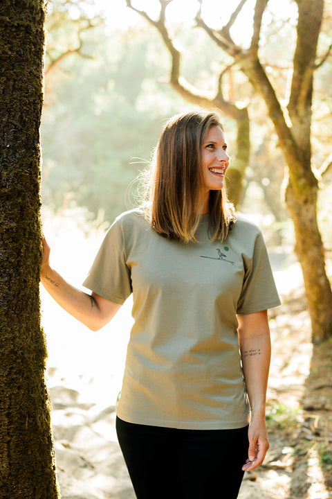 A woman wearing the Moment Women's Lt Dan T-Shirt - Eucalyptus touching a tree in the forest.