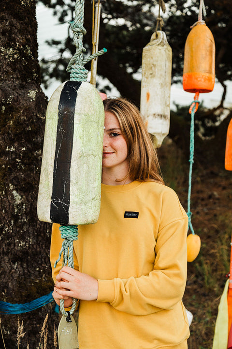Moment Women's Sunset Pullover Crew - Gold - Model holding onto hanging buoy