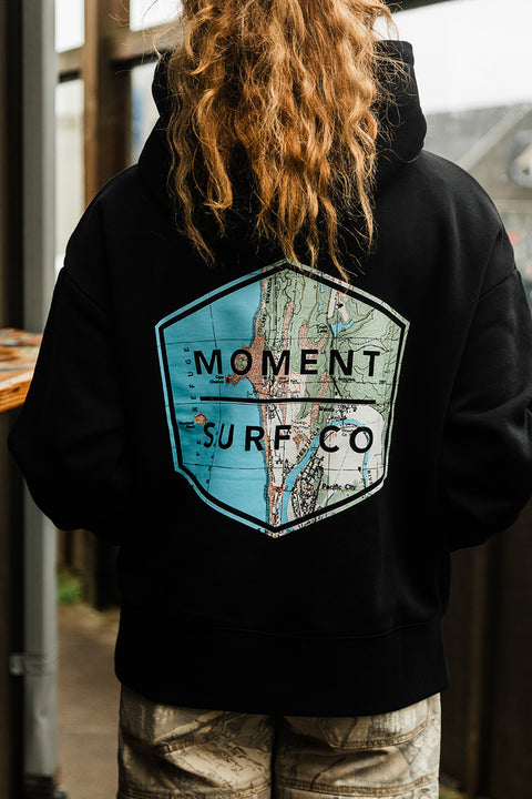 Moment Women's Boxed Topo Logo Pullover Hoodie - Black / Multi on model facing away from the camera showing the back logo of the hoodie