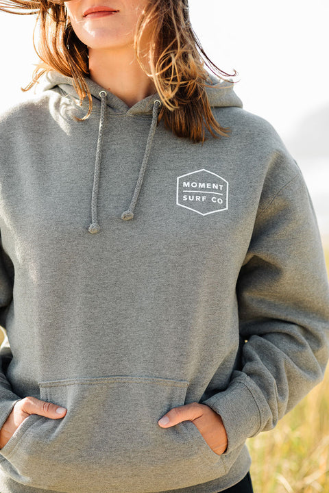 A woman wearing the Moment Boxed Topo Logo Pullover Hoodie - Gunmetal Heather facing towards the camera.