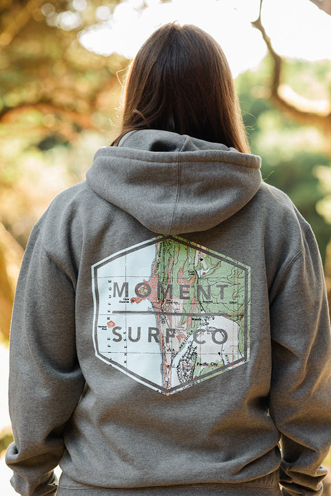 A woman wearing the Moment Boxed Topo Logo Pullover Hoodie - Gunmetal Heather facing away from the camera.